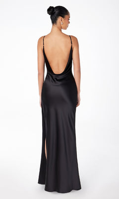 A woman stands with her back to the camera in the Astee T2000 Cowl-Back Sexy Long Prom Dress, a sleek black evening gown with thin straps and a low back, her hair neatly styled in a bun.