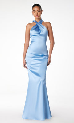 A woman stands against a white background, wearing the Astee T2005—an elegant, form-fitting light blue satin prom dress with a crisscross halter neckline, perfect for formal events.