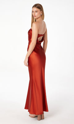 Model wearing the Astee T2006 Strapless Long Satin Maxi Prom Dress, featuring a shiny rust color and open back, as she stands against a plain white background looking over her shoulder.