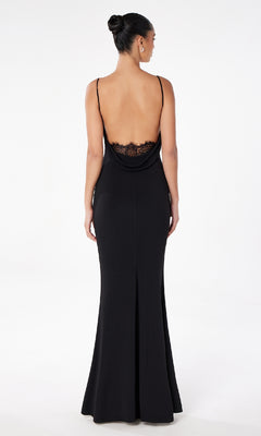 A woman models the Astee T2008 Cowl Open-Back Long Prom Dress, a black spaghetti-strap formal gown with lace detail, standing against a plain white background and facing away from the camera.