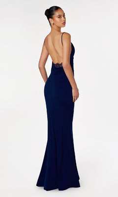 Woman wearing the Astee T2008 Cowl Open-Back Long Prom Dress in navy blue, featuring spaghetti straps and an open back, standing on a white background and looking over her shoulder.