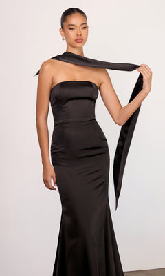 A woman in a black Choker-Sash Strapless Long Prom Dress (Astee T2012) stands against a plain backdrop, holding a long matching sash over her shoulder.