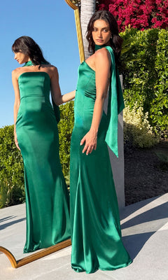 A woman in the Choker-Sash Strapless Long Prom Dress: Astee T2012 poses outdoors by a mirror reflecting her back. Surrounded by lush greenery and pink flowers, she showcases the elegance of this green satin evening gown.