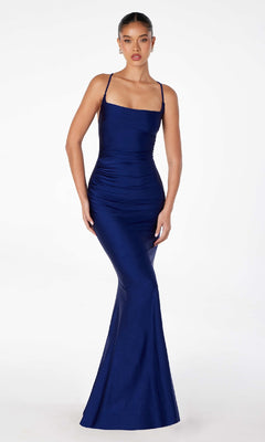 A woman stands against a white background wearing the Strappy Open-Back Long Prom Dress: Astee T3001, a fitted, floor-length navy gown with thin straps.