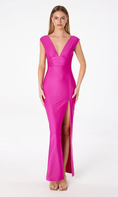 A woman faces forward in the Empire-Waist Long Jersey Prom Dress: Astee T5000, a sleeveless hot pink gown with a deep V-neckline, empire waist, high front slit, and nude heels, set against a plain white background.