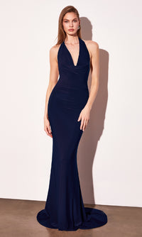Woman modeling a long halter navy  blue evening gown with a cowl neckline in front of a white wall.