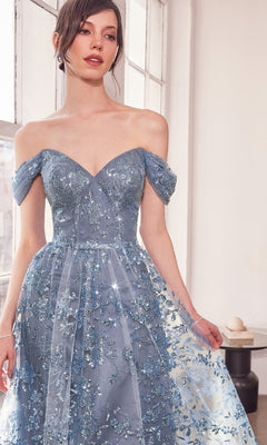 A woman in the Amoris T607 long glitter-print prom dress stands by a large window indoors, her light blue gown sparkling softly in the light.