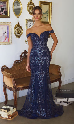 A woman in the Amoris T613 off-shoulder sequin prom gown in navy stands gracefully before a vintage sofa and framed wall art.