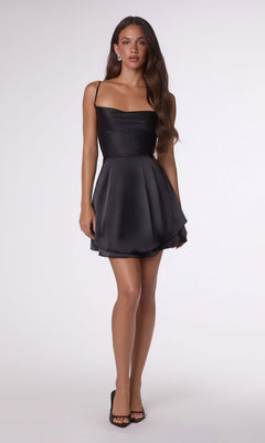 A woman stands against a plain background wearing the Amoris T616 Short Homecoming Dress—black satin with thin straps, an open back, a subtle A-line skirt—and black open-toe heels.