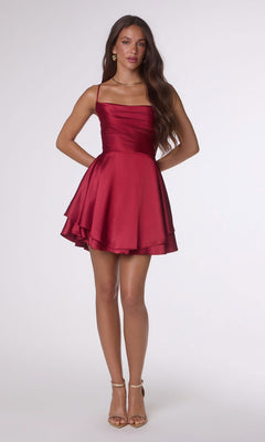 A woman wears the Amoris T616 short homecoming dress, featuring a sleeveless red satin design with an A-line skirt and fitted bodice, styled with nude high-heeled sandals.