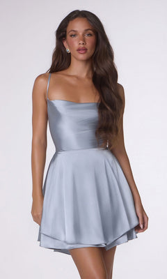 A woman with long brown hair wears the Amoris T616 short homecoming dress in dusty blue, featuring thin straps, an open back, and a flared A-line skirt, standing against a plain light background.