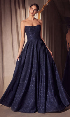 A woman stands in front of a curtain and mirror wearing the Strapless Long A-Line Glitter Prom Dress: Amoris T701, which features a strapless neckline, full A-line skirt, and subtle sparkling details.