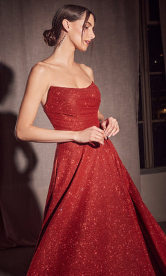 A woman in the Amoris T701 Strapless Long A-Line Glitter Prom Dress in red stands indoors by a window, her hair styled in a low bun.