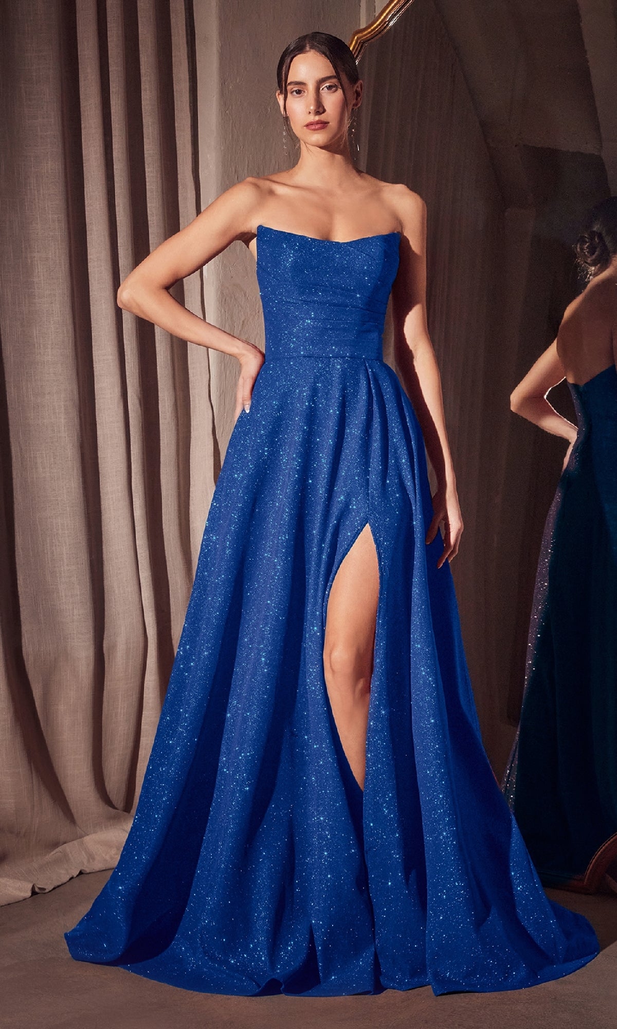 A woman stands indoors wearing the affordable Amoris T701, a strapless, floor-length A-line glitter prom dress in sparkling blue with a thigh-high slit.