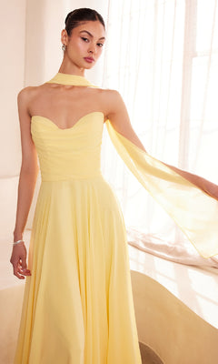 A woman in a Strapless Long Chiffon Prom Dress: Amoris T703 with a matching scarf stands by a sunlit window, highlighting this elegant and affordable formal dress, ideal for special occasions.