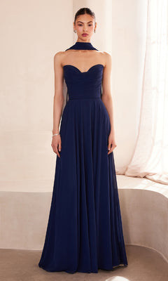 Indoors, a woman wears the Strapless Long Chiffon Prom Dress: Amoris T703—a floor-length navy blue gown with a matching neck scarf.
