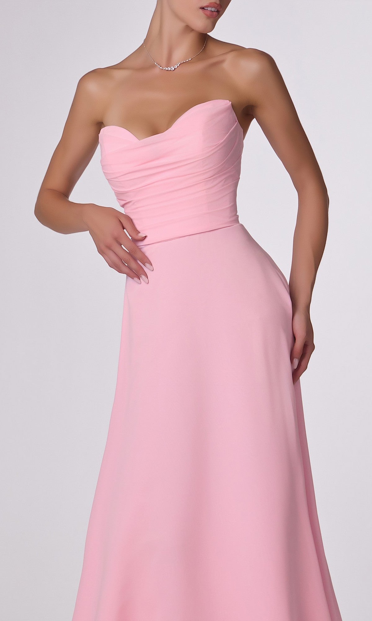 A woman in the Strapless Long Chiffon Prom Dress: CLT703, featuring a light pink corset-style bodice, slight pleating, an elegant A-line skirt, and accessorized with a delicate necklace.