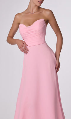 A woman in the Strapless Long Chiffon Prom Dress: CLT703, featuring a light pink corset-style bodice, slight pleating, an elegant A-line skirt, and accessorized with a delicate necklace.