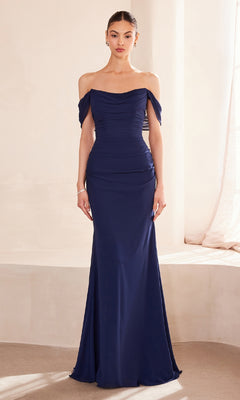 A woman stands indoors wearing the Off-Shoulder Classic Prom Gown: Amoris T705—a floor-length, navy blue dress with draped off-the-shoulder sleeves and a fitted bodice.