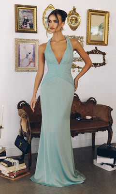 A woman in a mint Long Prom Dress: Amoris T720 with a satin skirt and ruched bodice stands by a vintage sofa, surrounded by framed wall art, books, and accessories.