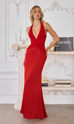 A woman wearing the Amoris T720 Long Prom Dress in red stands indoors by a white ornate mantel, with candles and books behind her.