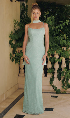 A woman in the Amoris T725 Long Prom Dress in sage, featuring delicate spaghetti straps and lace details, stands on a tiled floor before a stone railing and lush green foliage.