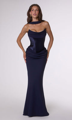 A woman poses against a plain light background wearing the Amoris T732 Long Prom Dress in navy, featuring a form-fitting stretch satin design with a draped neckline, corset back, and floor-length skirt.