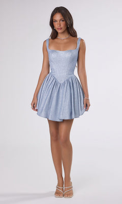 A woman poses against a white background in the Amoris T738 short homecoming dress in Paris Blue, featuring a shimmering stretch fabric and fit-and-flare silhouette, styled with strappy heels and minimal jewelry.