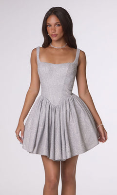 A woman stands against a plain light background wearing the Amoris T738 Short Homecoming Dress in silver, featuring a sleeveless design and a flared, short skirt.
