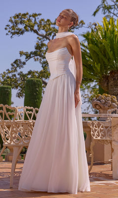 A woman in the Amoris T741W long prom dress, featuring an off-white strapless satin bodice and chiffon A-line skirt, stands on a patio near wrought iron chairs with her eyes closed, surrounded by greenery and trees.