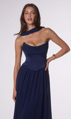 A woman poses against a plain light background, wearing the Amoris T741 Long Prom Dress—a navy blue, off-the-shoulder gown featuring a draped neckline and a fitted satin corset bodice.