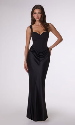 A woman poses against a plain background in the Amoris T742 Long Prom Dress in black, showcasing its sleek, form-fitting silhouette, thick straps, structured crepe bodice, floor-length hem, and subtle hip drape.