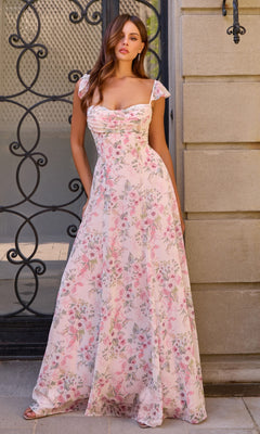 A woman stands in front of a decorative black iron gate and stone wall, wearing the Amoris T749 Long Prom Dress—a beautiful light pink floral gown with cap sleeves and a flowing chiffon A-line skirt that enhances the romantic setting.