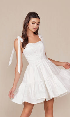 Model wearing the Shoulder-Tie Little White Party Dress T869W, a sleeveless short white dress with tie straps, posed against a plain beige background.