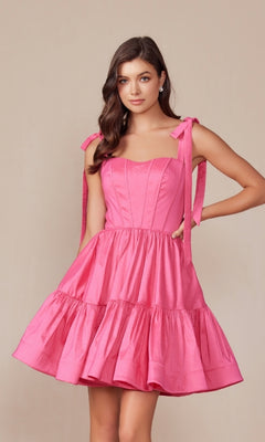 A woman wears the Shoulder-Tie Short Lace-Up A-Line Hoco Dress T869, a sleeveless pink party dress with tied shoulders and flared skirt, standing against a plain beige background.