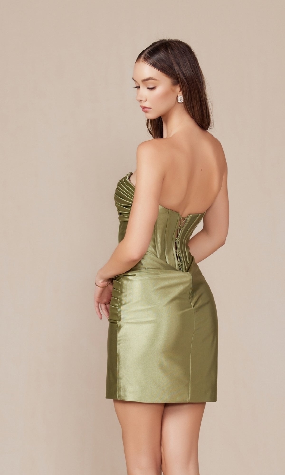 A woman stands against a plain background wearing the Lace-Up Strapless Cut-Out Short Hoco Dress T871 in olive green satin, featuring a corset bodice, lace-up back, and strapless short design, looking to the side.