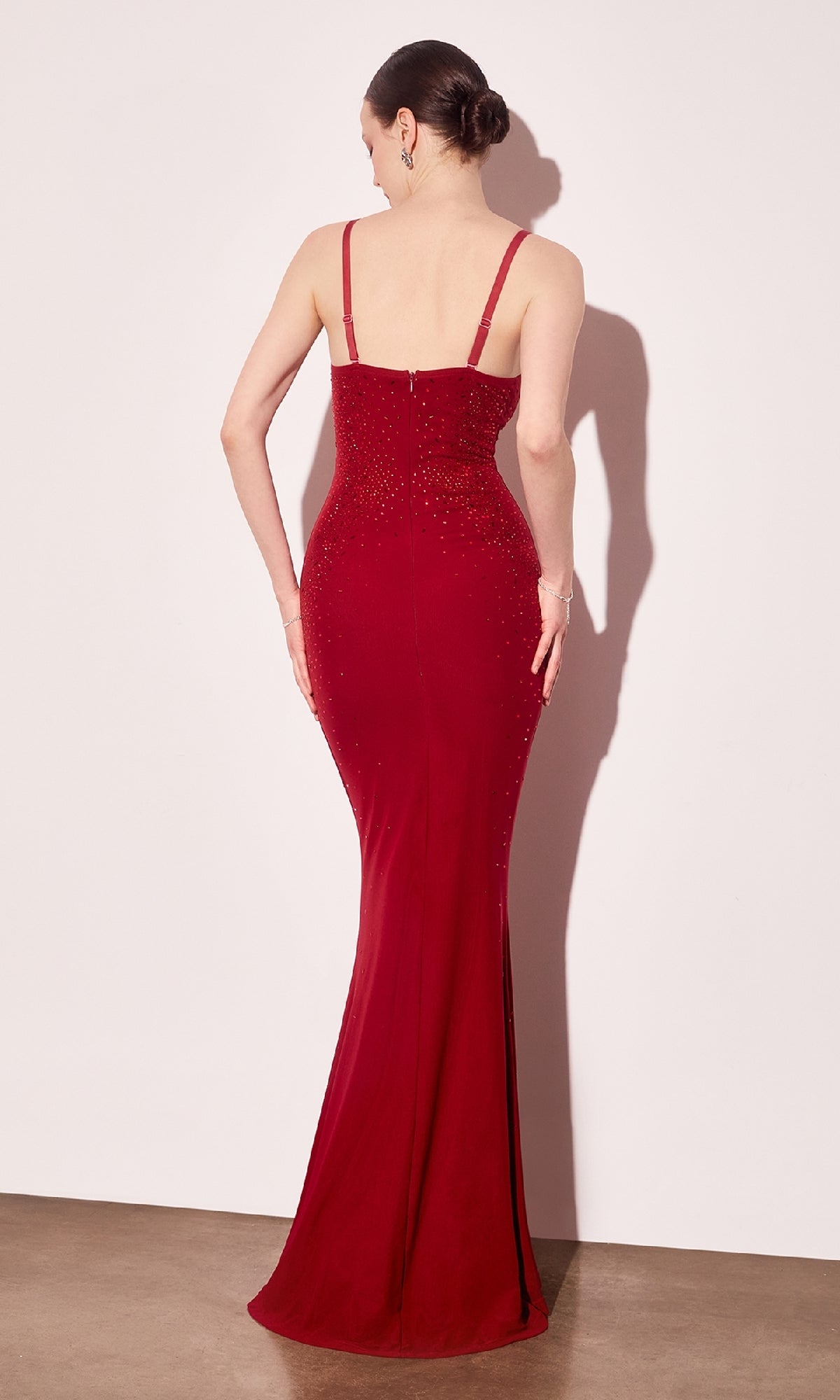 Woman modeling the back of a floor length red evening gown with a zipper back closure in front of a white wall.