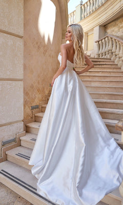 A woman wearing the Strapless Off-White Bridal Gown: Tina Holly TA611W stands on a stone staircase, facing away and looking over her shoulder.