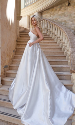 A woman wearing the Strapless Off-White Bridal Gown: Tina Holly TA611W stands on a curved stone staircase, with a brick wall and balustrade in the background.