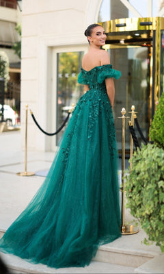 A woman wearing the Tina Holly TE231 emerald green prom dress with off-the-shoulder sleeves and floral details stands outside a building, looking back and smiling.