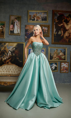 A woman stands indoors in a Long Formal Dress: Tina Holly TE706 in soft mint, its strapless embroidered corset bodice and ball gown skirt beautifully complementing the wall adorned with framed classical paintings.