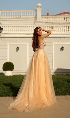 A woman in the Long Formal Dress: Tina Holly TE708, a flowing strapless glitter ball gown, stands on a paved path before a white building with decorative railings, looking over her shoulder.