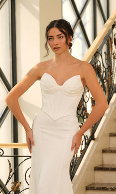 A woman stands on a staircase in the Contemporary Wedding Dress: Tina Holly TE709, featuring a strapless, white fitted bodice with a slight sweetheart neckline that embodies minimalist elegance.