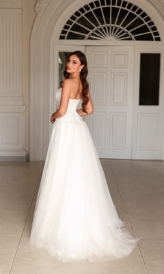 A woman wearing a strapless, floor-length Tina Holly TE710 fairytale wedding dress with a full tulle skirt looks over her shoulder.