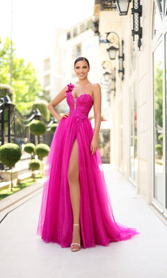 A woman stands outdoors in the Tina Holly TK554, a bright pink one-shoulder glitter prom gown with a high slit, posing on a walkway beside a decorative fence and manicured bushes.