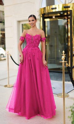 A woman stands outside a building wearing the Long Prom Dress: Tina Holly TK582, an off-the-shoulder, floor-length gown in bright pink with 3D flower appliques and a sheer overlay, resembling stunning glitter tulle.