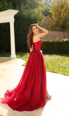 A woman in the Tina Holly TK801 long formal dress with a strapless mikado corset bodice stands on a sunlit patio, framed by greenery and a white column in the background.