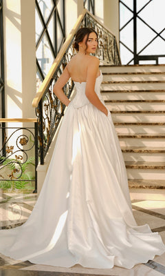 A woman in the Off-White Satin Wedding Dress: Tina Holly TK803, featuring a strapless neckline, a-line skirt, and long train, stands on an elegant staircase looking over her shoulder.