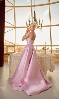 A woman wearing the Long Formal Dress: Tina Holly TK804, a strapless mikado gown with an elegant A-line skirt, stands before a large window and chandelier, with a draped table set with candles behind her.