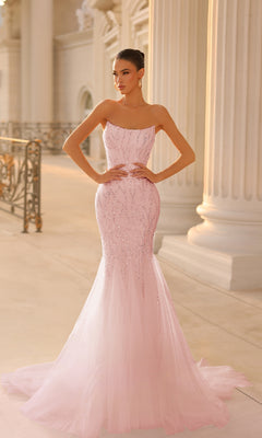 A woman in the Strapless Long Glitter Prom Gown: Tina Holly TK807—an elegant, fitted light pink dress with a flared tulle skirt and beaded accents—stands in a grand hall adorned with columns.